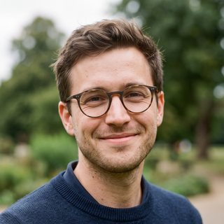 Elias Brandt in a park, wearing round glasses and a navy jumper